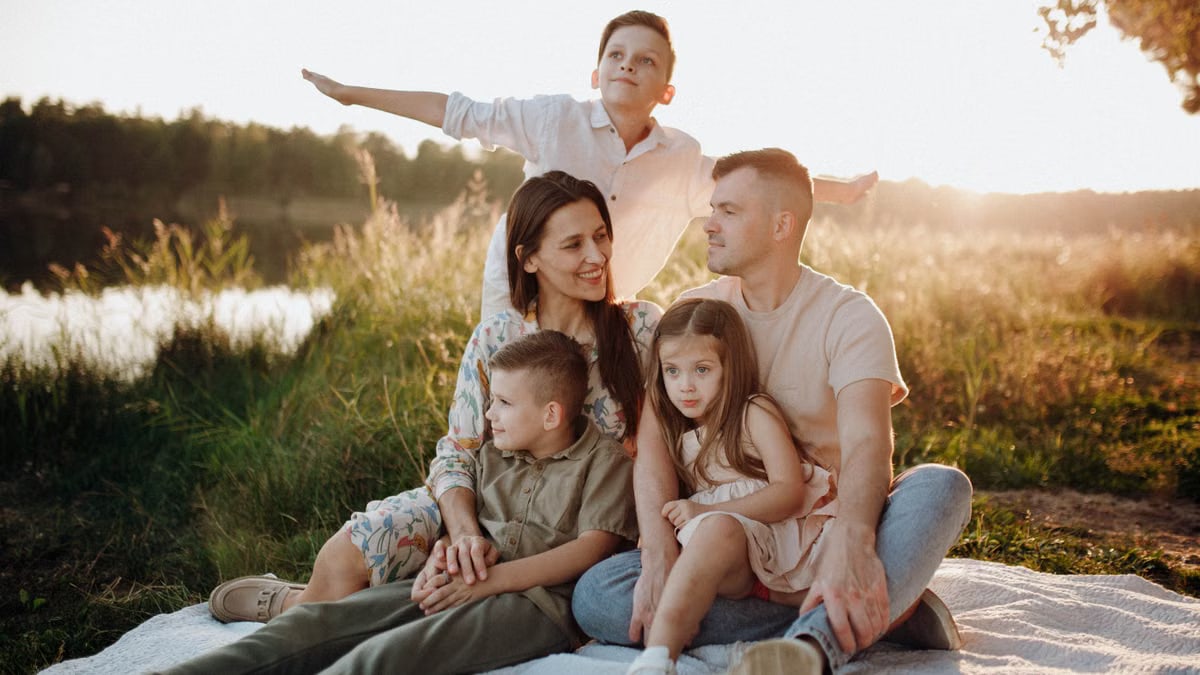 A family of five enjoying a serene picnic in a sunlit meadow during sunset.